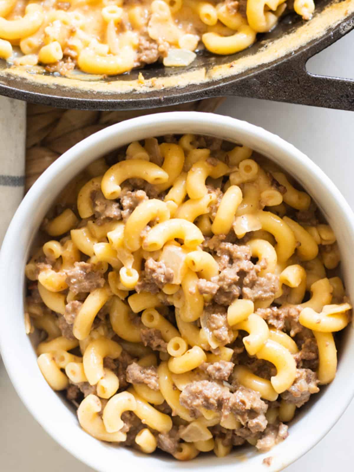 A bowl of gluten-free hamburger helper with a skillet of hamburger helper in the background.