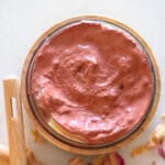A jar of homemade rose clay face mask with rose petals around it.