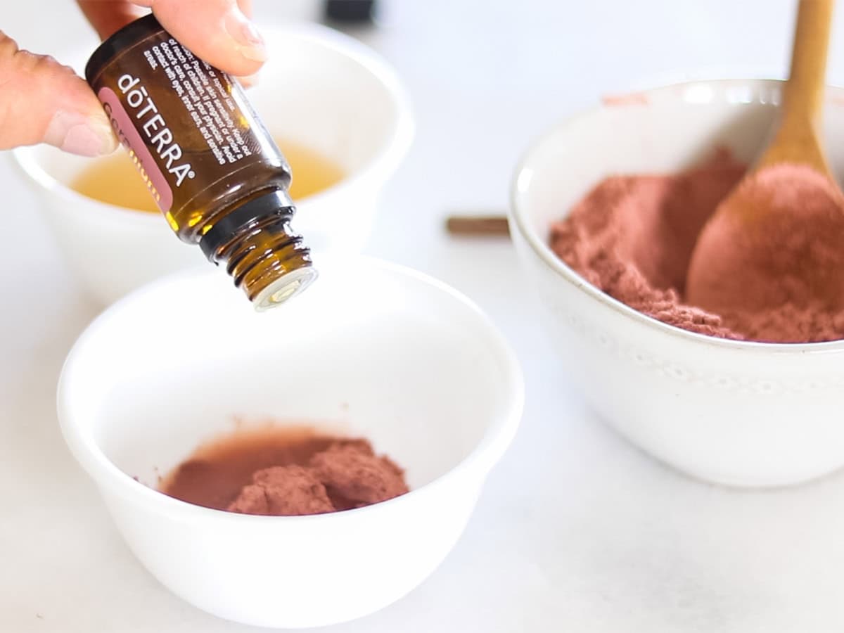 Dropping essential oil into a bowl of rose clay face mask.
