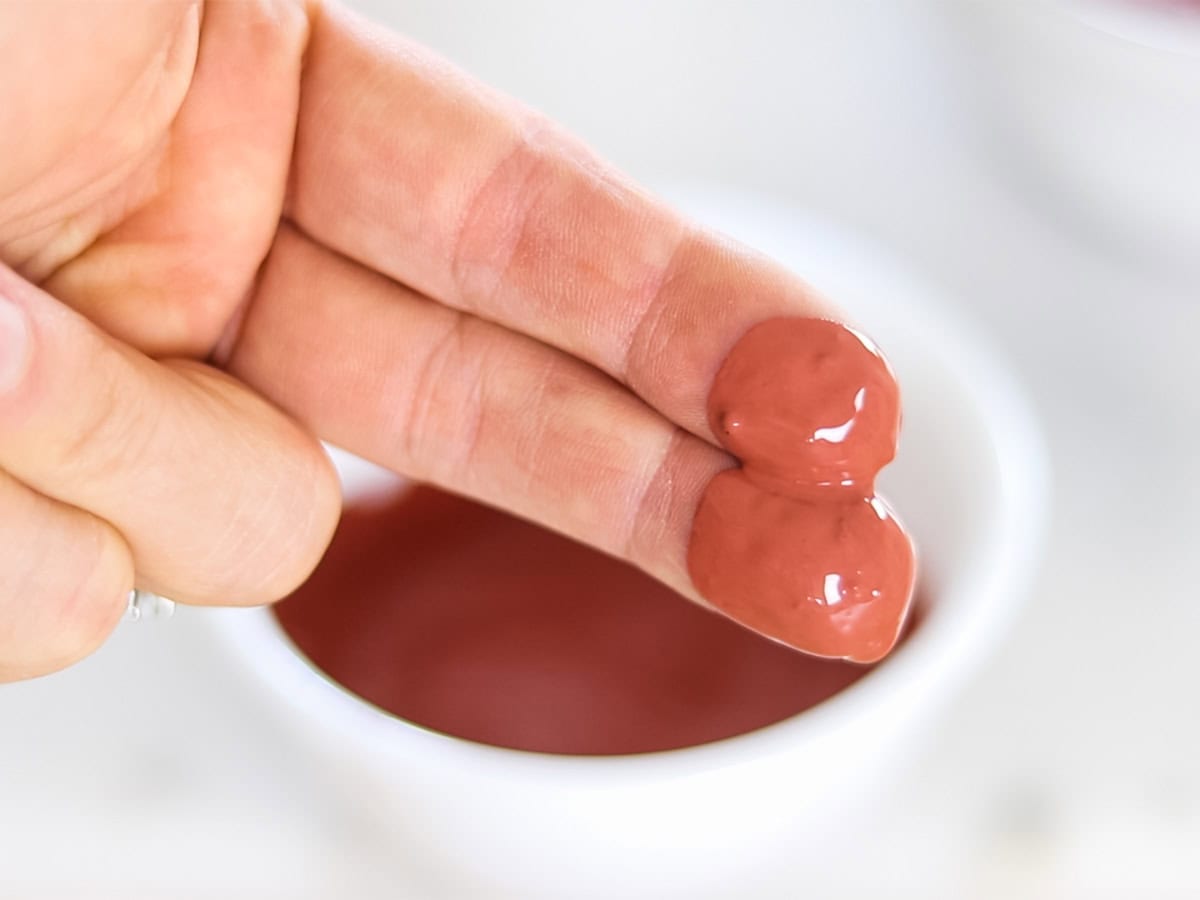 Two fingers dipped in a bowl of rose clay face mask. 