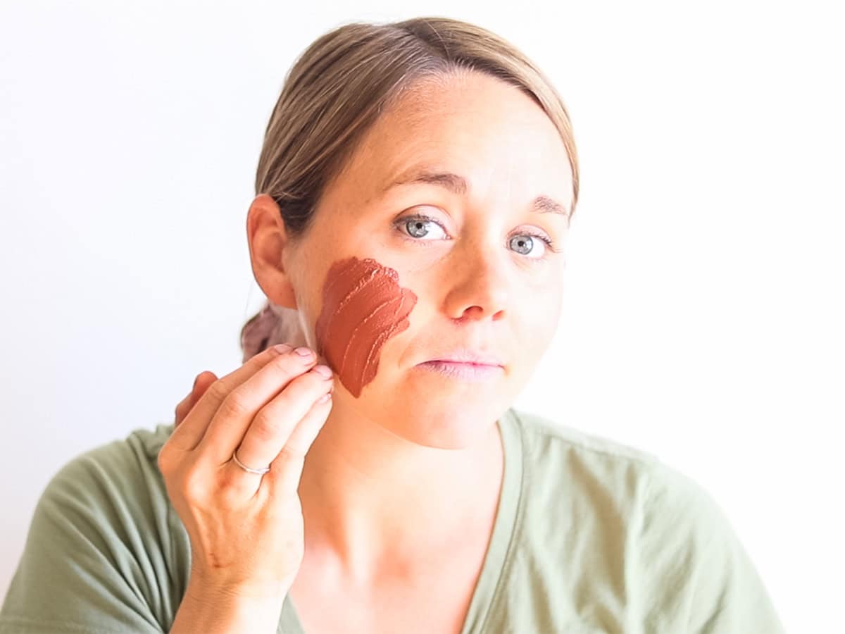 Laura spreading rose clay face mask onto her face. 