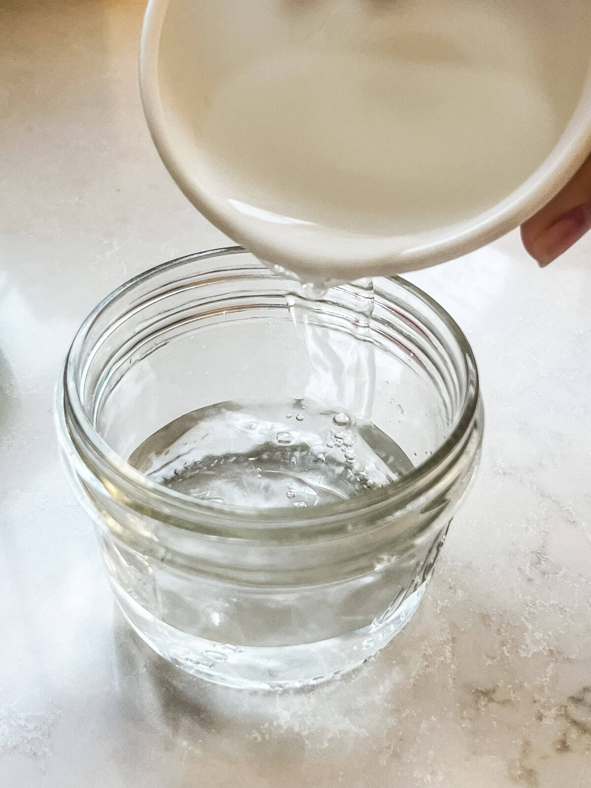 Pouring water into a small glass mason jar. 