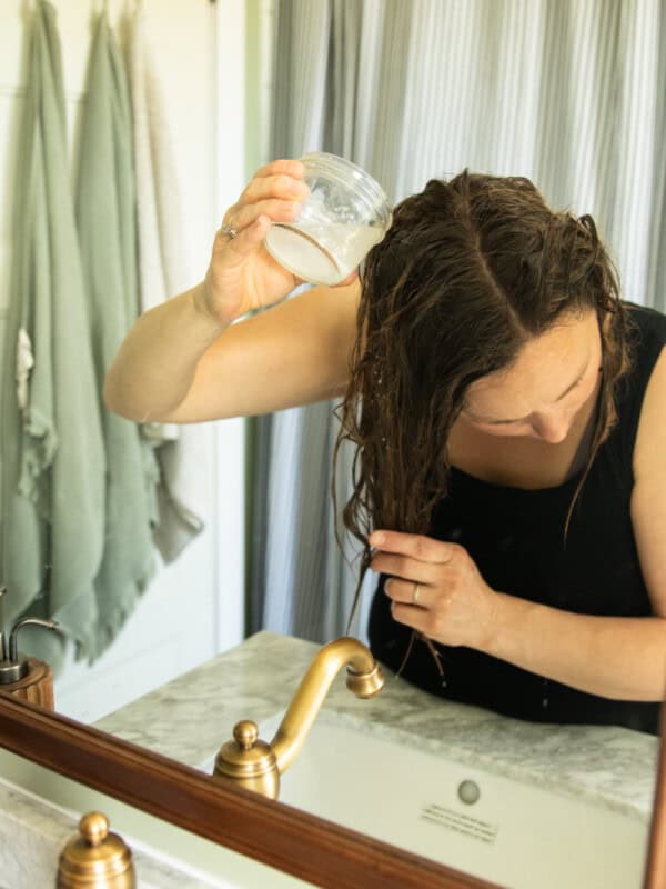Pouring baking soda hair rinse into the hair over a bathroom sink.