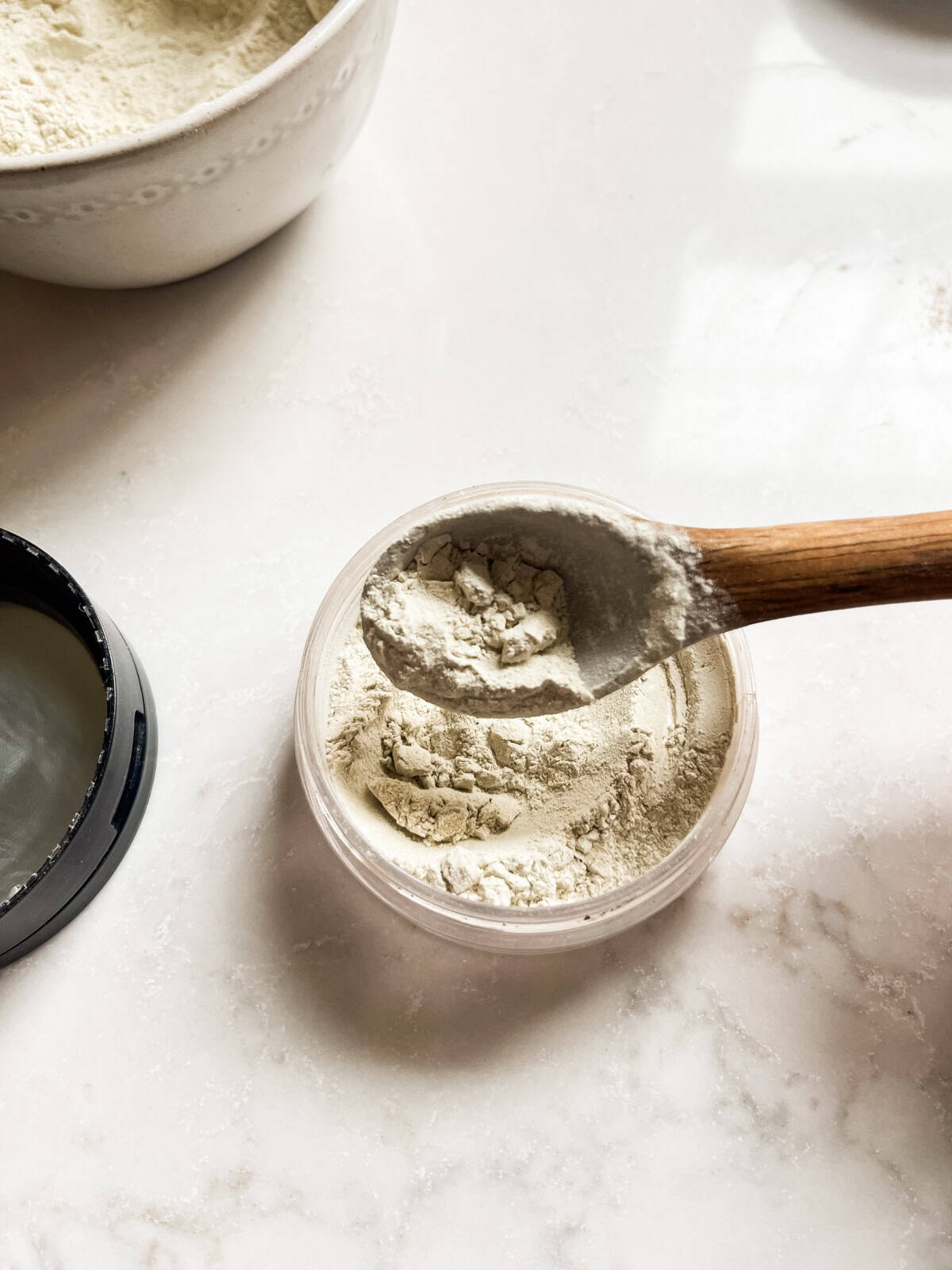 Scooping body powder into a storage jar with a spoon. 