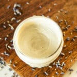 A jar of homemade diaper cream on a wooden board surrounded by lavender buds.