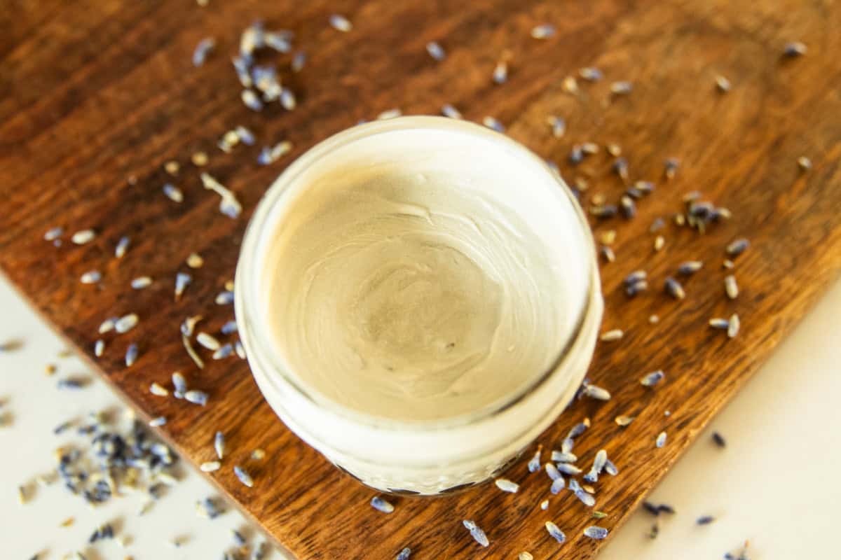 A jar of homemade diaper cream on a wooden board surrounded by lavender buds.