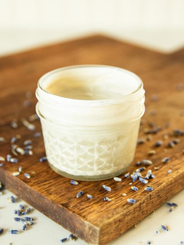 A jar of DIY diaper cream on a wooden board with lavender buds around it.