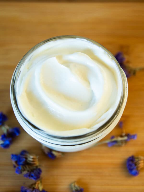 A jar of homemade goat milk lotion with dried flowers around it.
