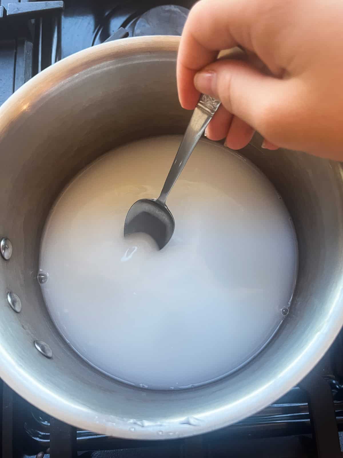 Stirring goat milk powder, water, and glycerin in a small saucepan. 