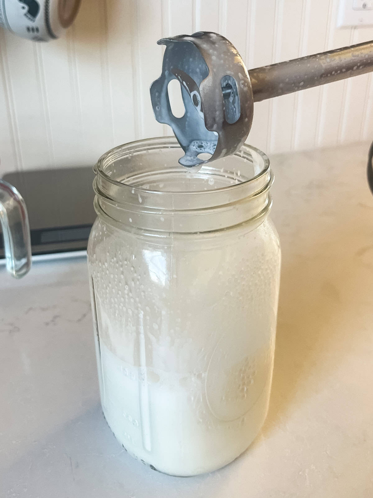 Mixing homemade lotion in a mason jar with an immersion blender.