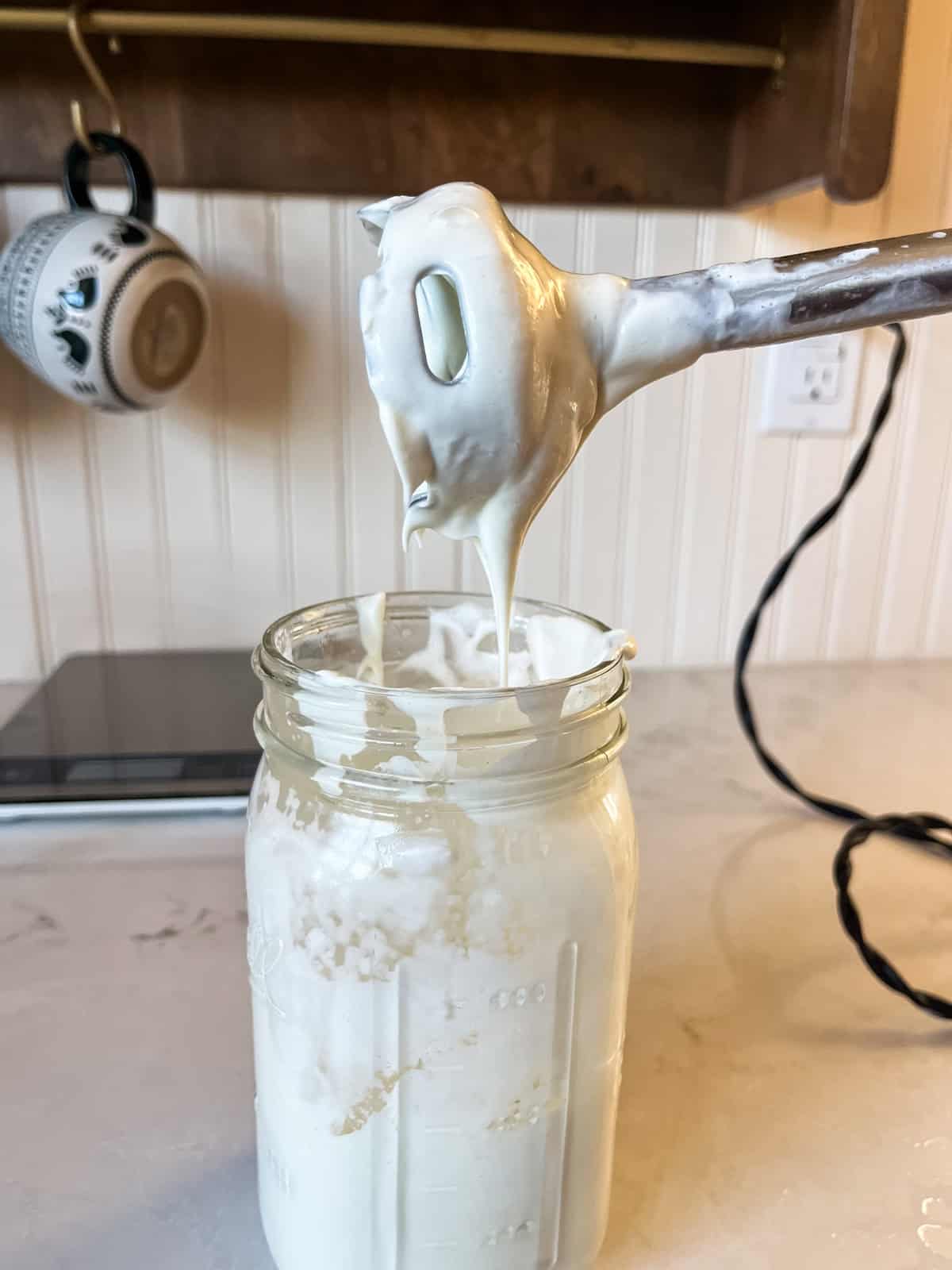 Blending homemade lotion in a mason jar with an immersion blender. The lotion is notably thicker than the previous photo.