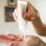 Squeezing homemade tallow lotion out of a squeeze bottle into the palm.