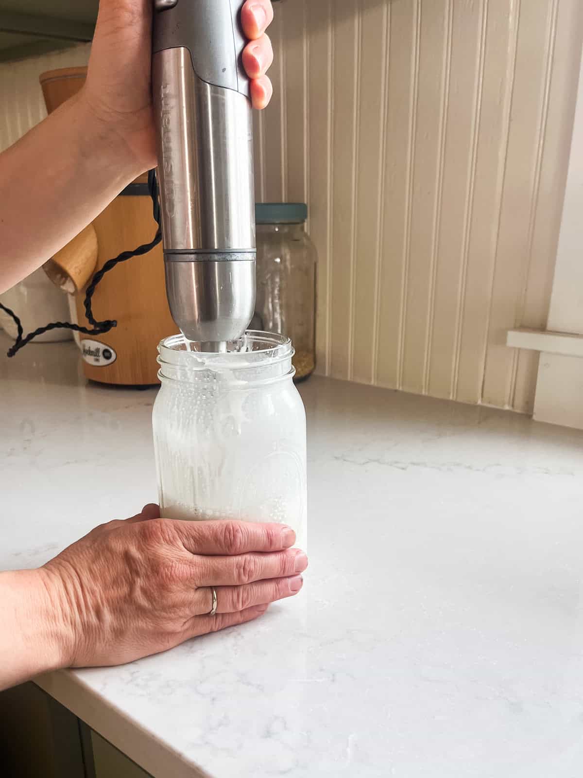 Blending a jar of homemade tallow lotion with an immersion blender.