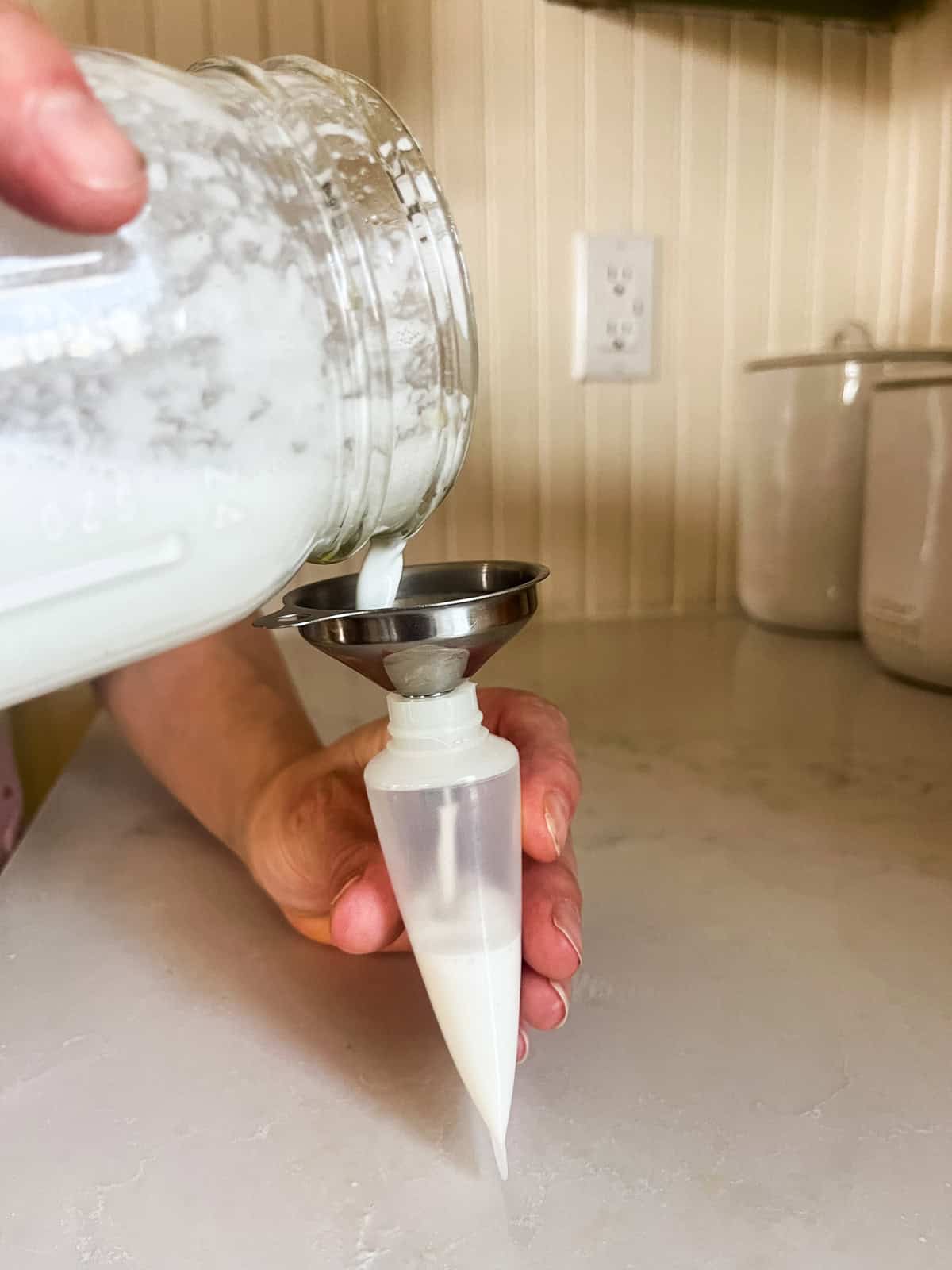 Pouring homemade tallow lotion into a squeeze bottle with a small funnel. 