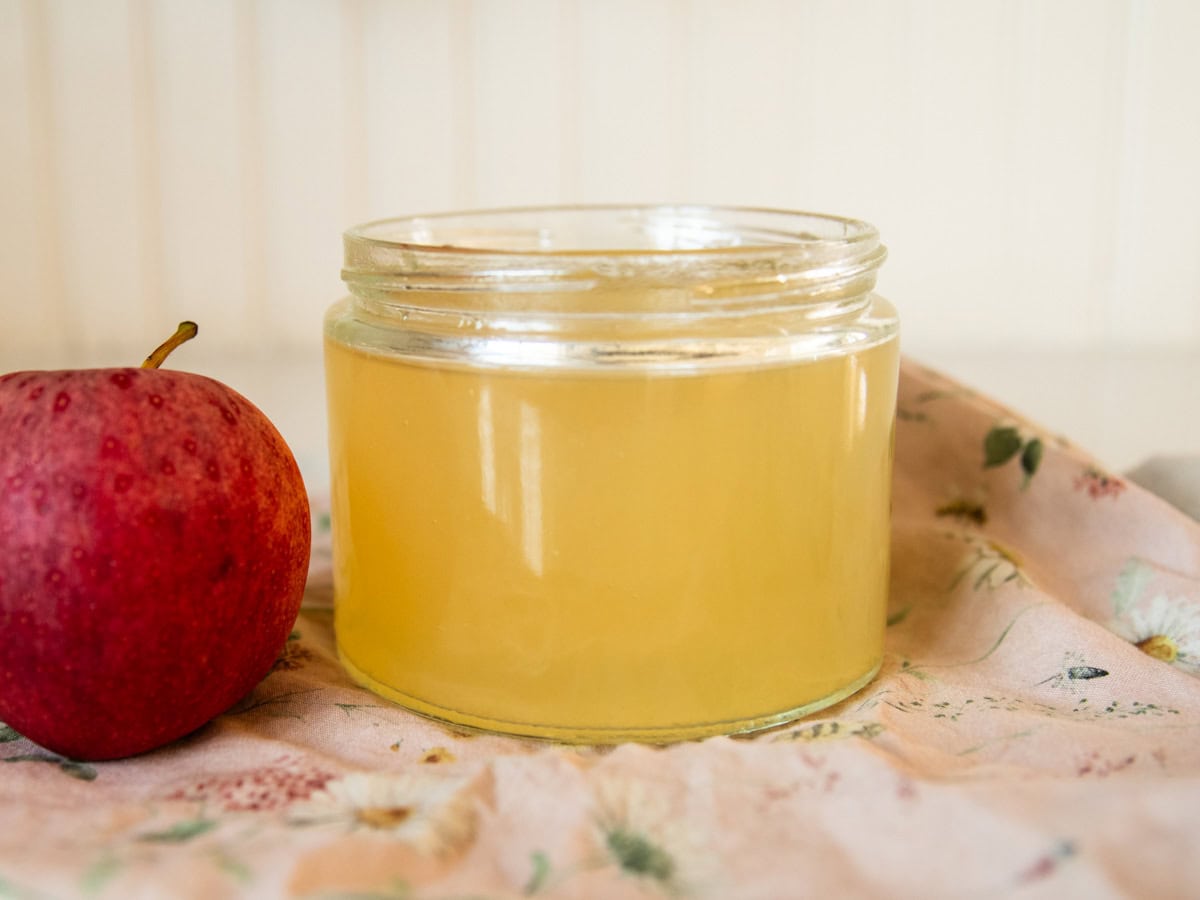 A jar of homemade apple cider vinegar next to an apple. 
