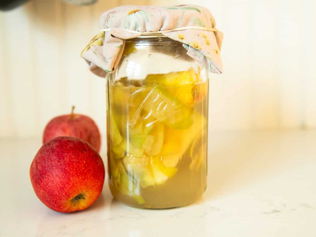 A jar of homemade apple cider vinegar with apples next to it.