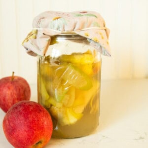 A jar of homemade apple cider vinegar with apples next to it.