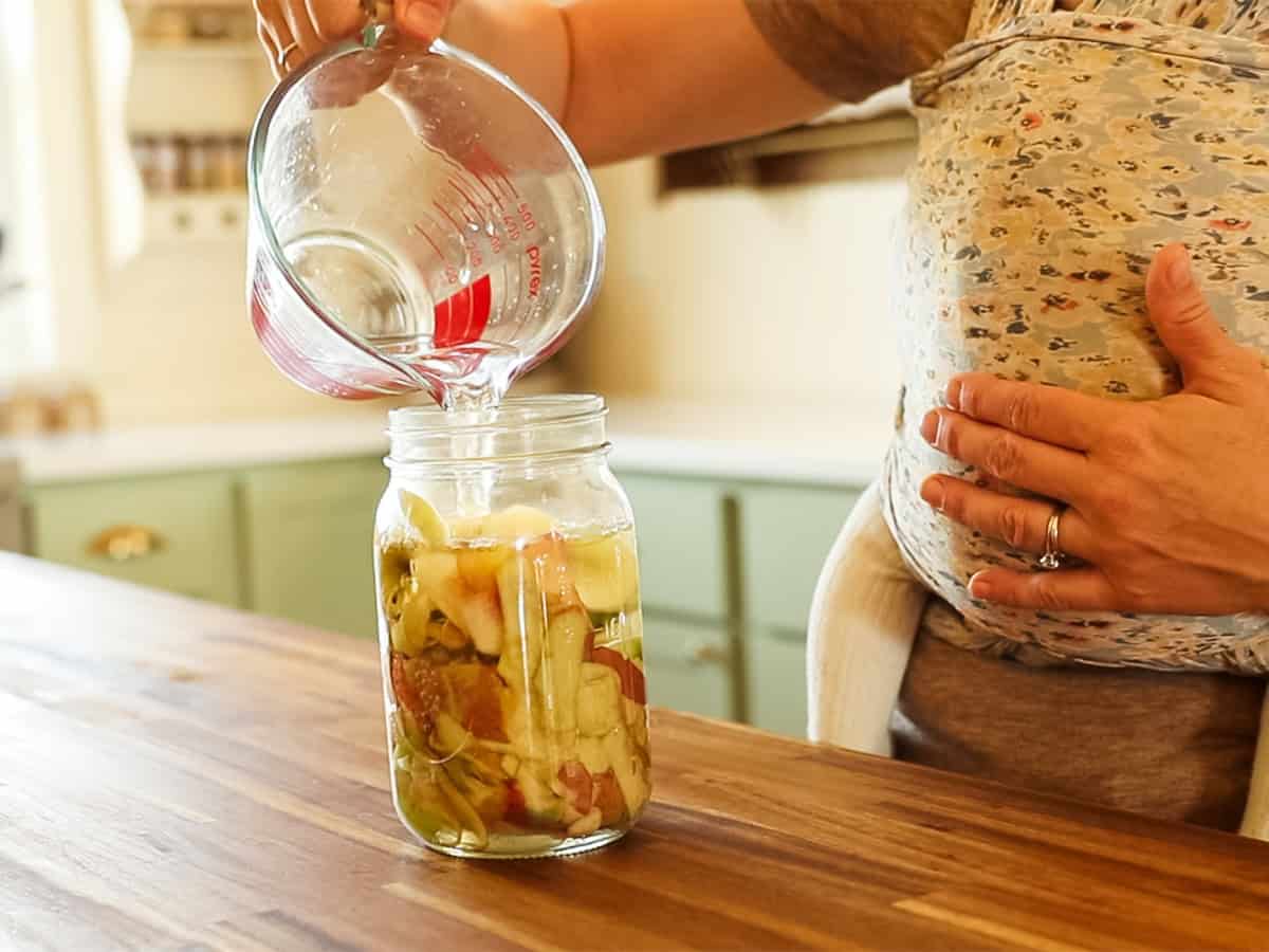 Pouring water into a jar of apple cider scraps.