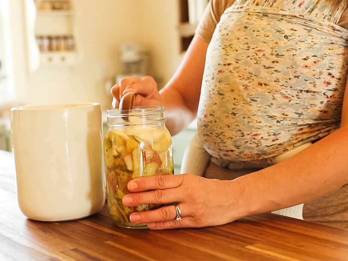 Adding sugar to the jar of apple scraps and water.