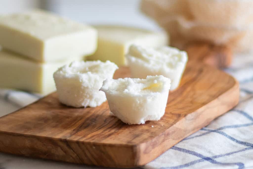 Three DIY bubble bath bars on a wooden board with soap bars in the background.