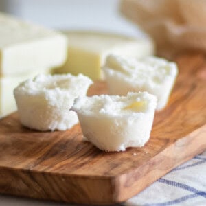 Three DIY bubble bath bars on a wooden board with soap bars in the background.
