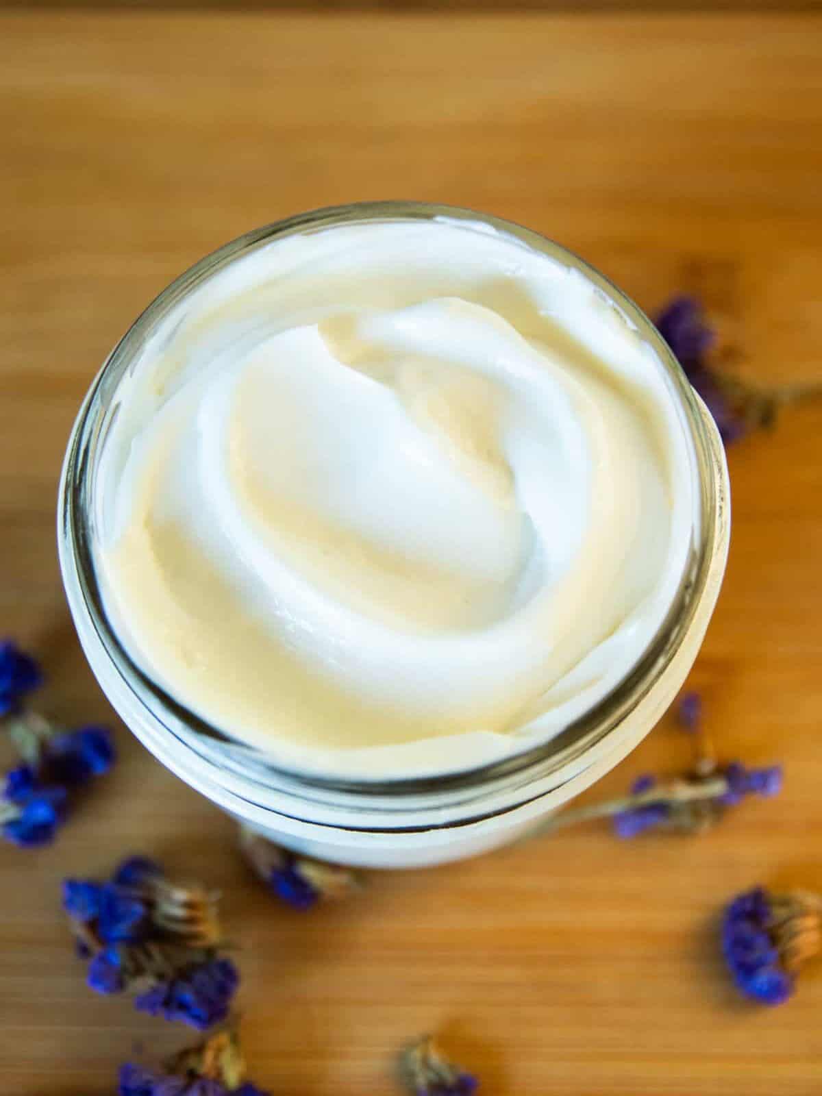 A jar of homemade goat milk lotion with dried flowers around it. 