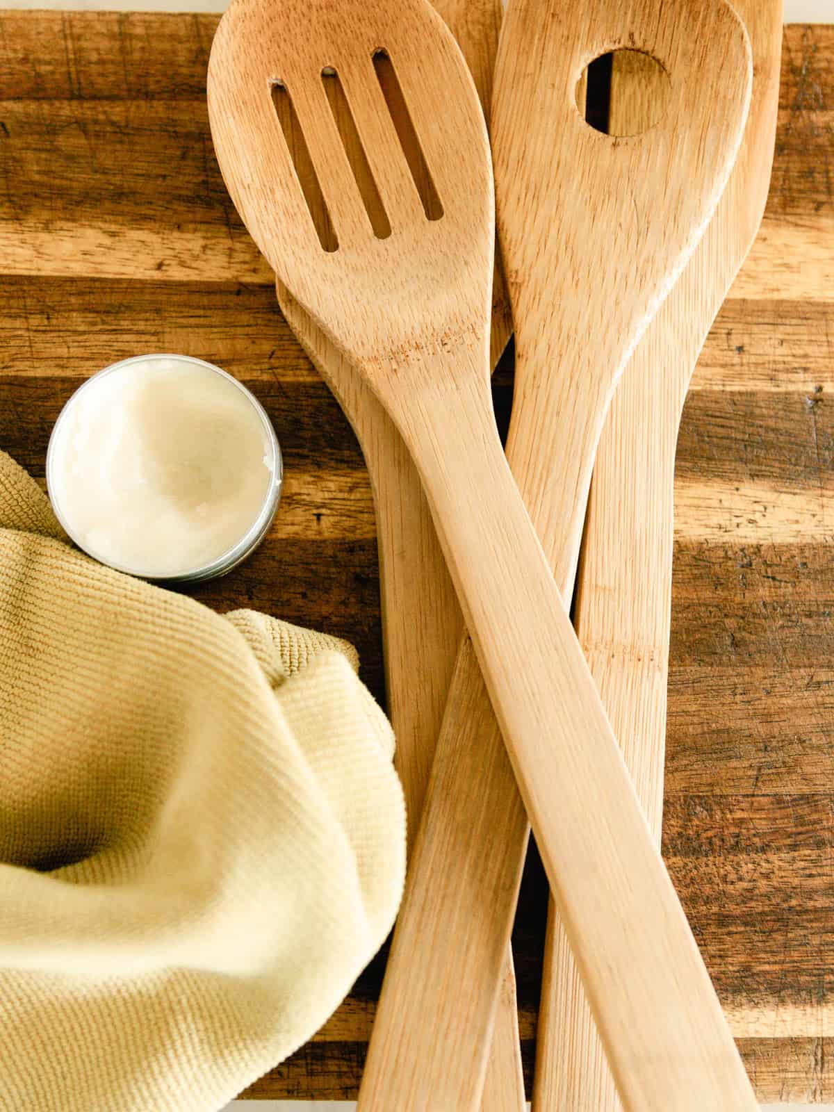 Homemade wood balm with a rag, wooden utensils, and a wooden cutting board.