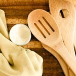 Homemade wood balm with a rag, wooden utensils, and a wooden cutting board.