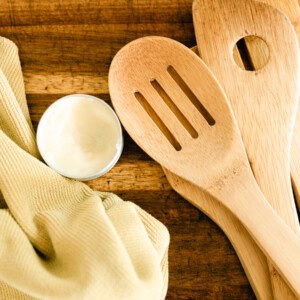 Homemade wood balm with a rag, wooden utensils, and a wooden cutting board.