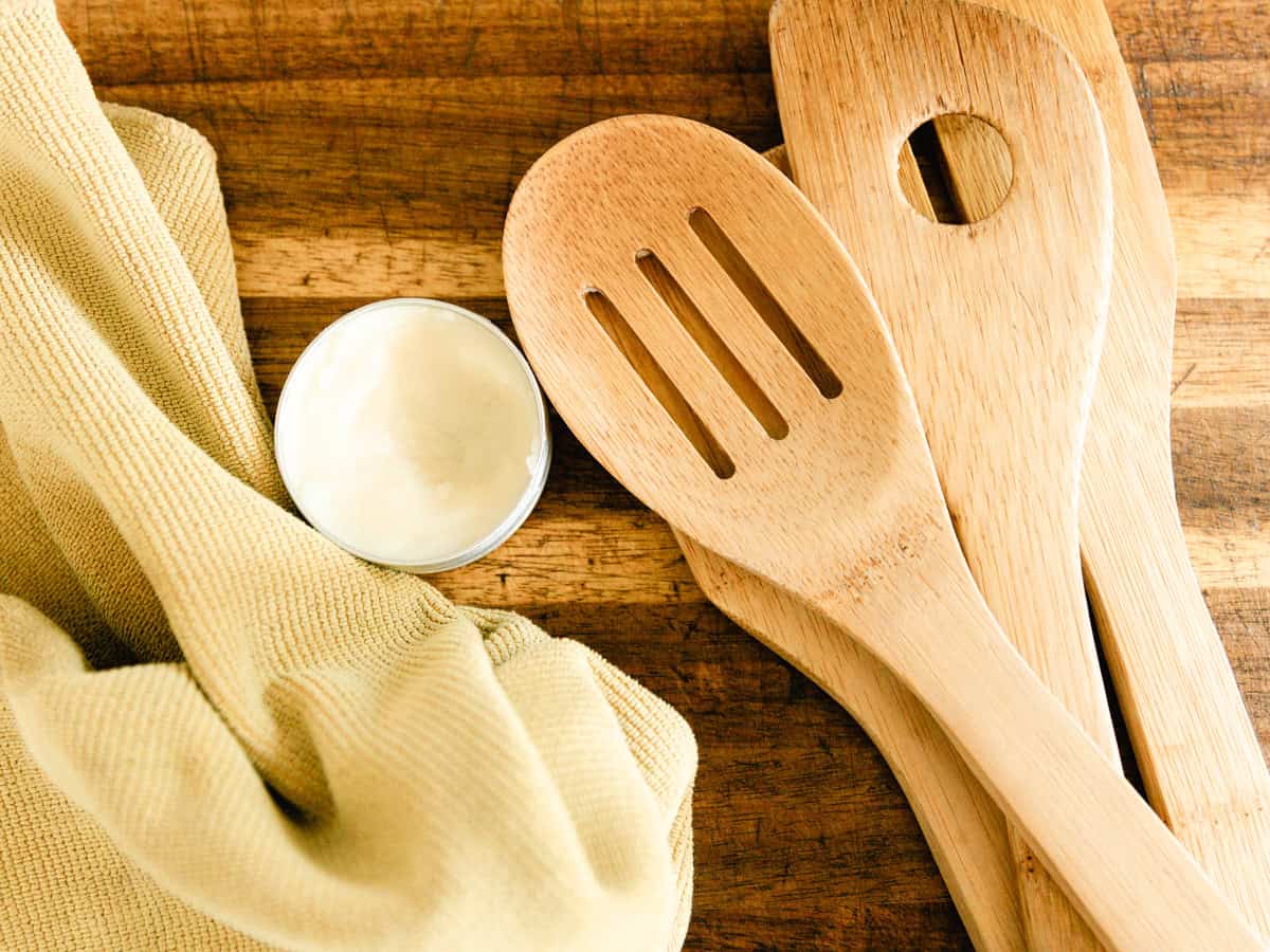 Homemade wood balm with a rag, wooden utensils, and a wooden cutting board.