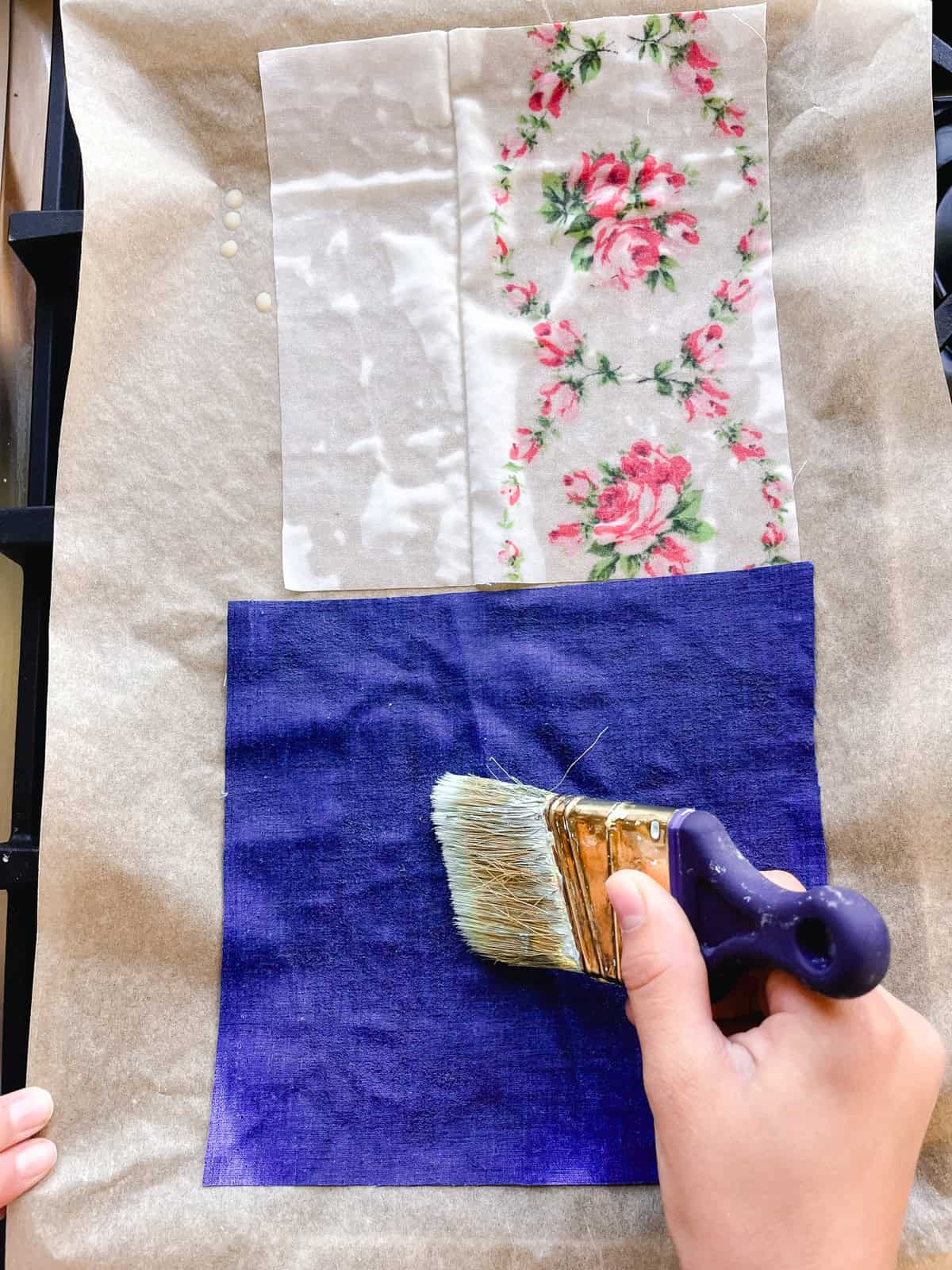 Using a paintbrush to spread melted beeswax evenly over the fabric. 