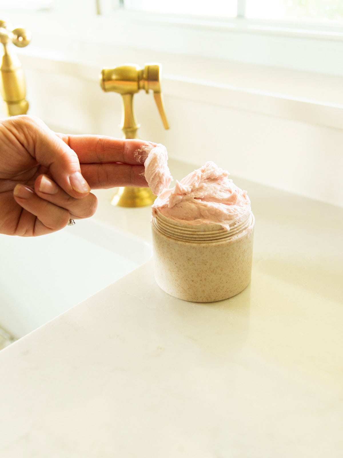 Scooping whipped foaming sugar scrub out of a jar at a sink. 