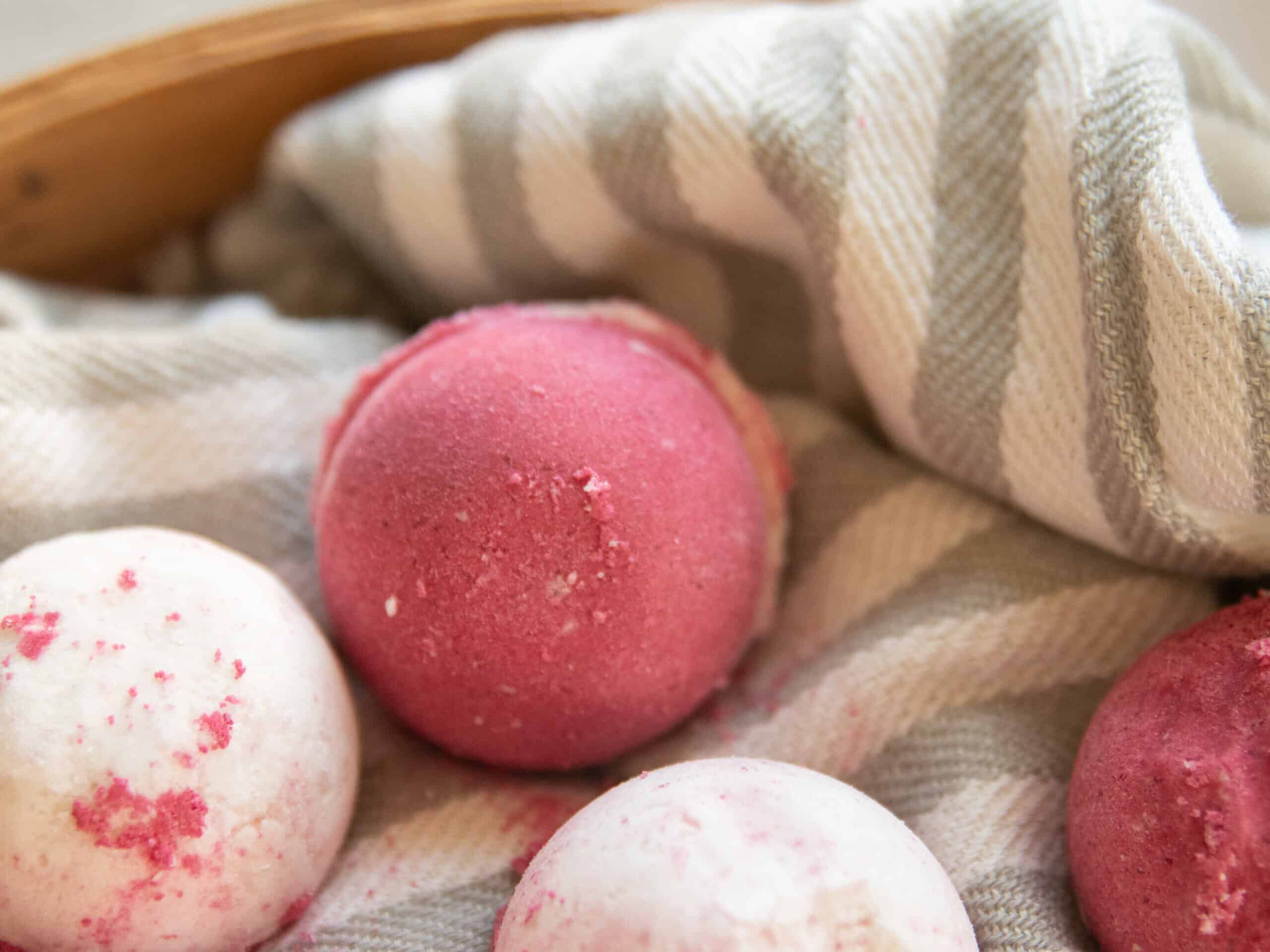 A close-up of a pink bath bomb on a striped towel. 