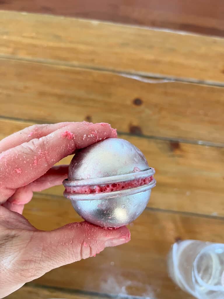 Pressing the two halves of a bath bomb mold together with bath bomb mixture inside.